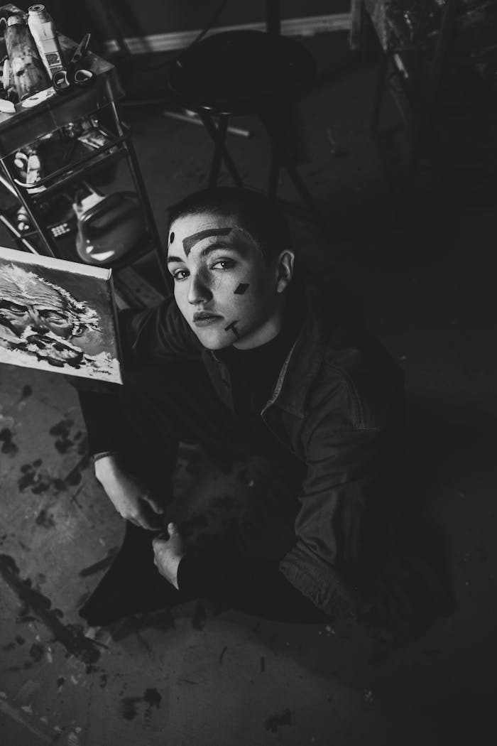 A captivating black and white portrait of a woman with face paint in an art studio, looking up.