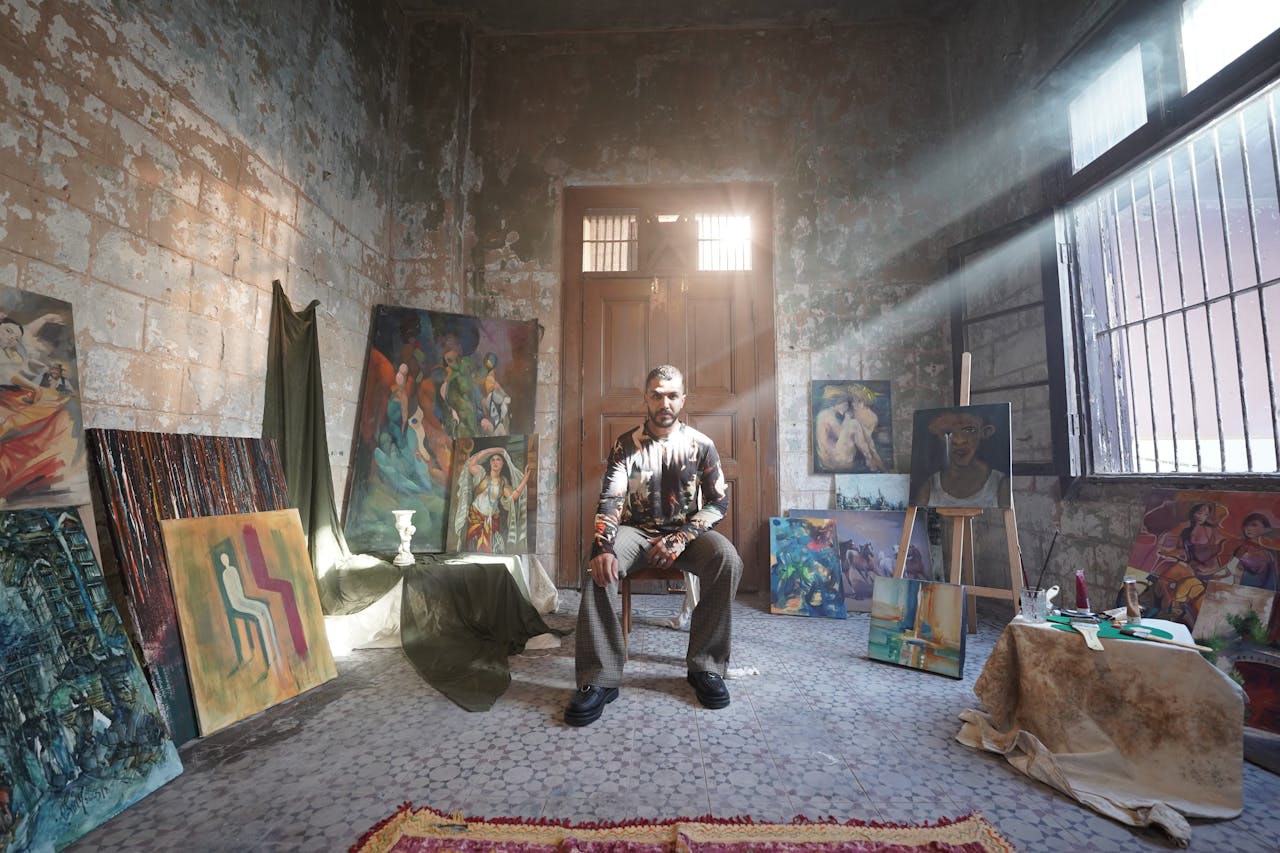Artist seated in a bright studio showcasing various colorful paintings.