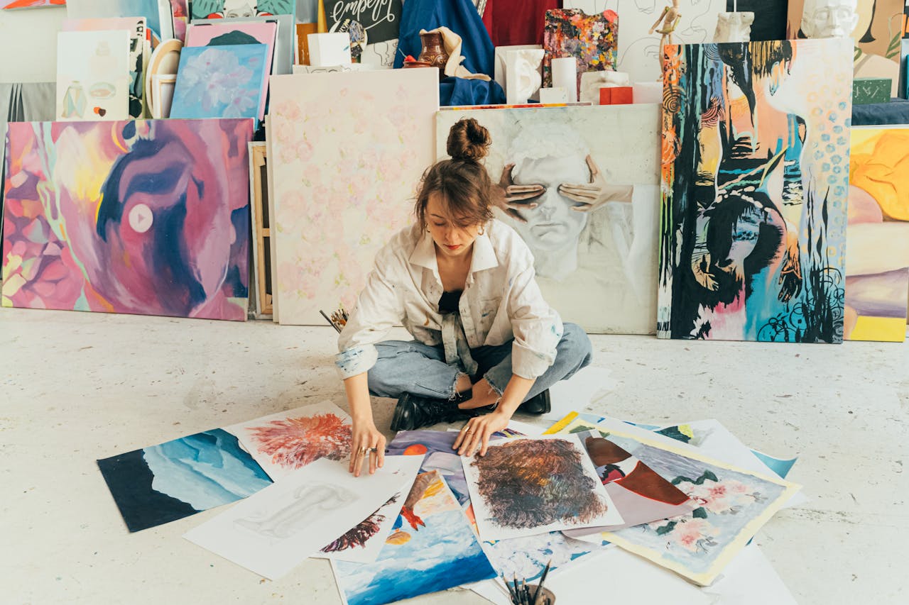 A woman artist organizes her paintings in a vibrant studio, surrounded by artwork and creativity.