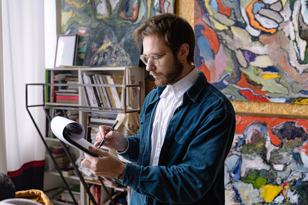 A focused artist sketching in a colorful studio filled with abstract paintings.
