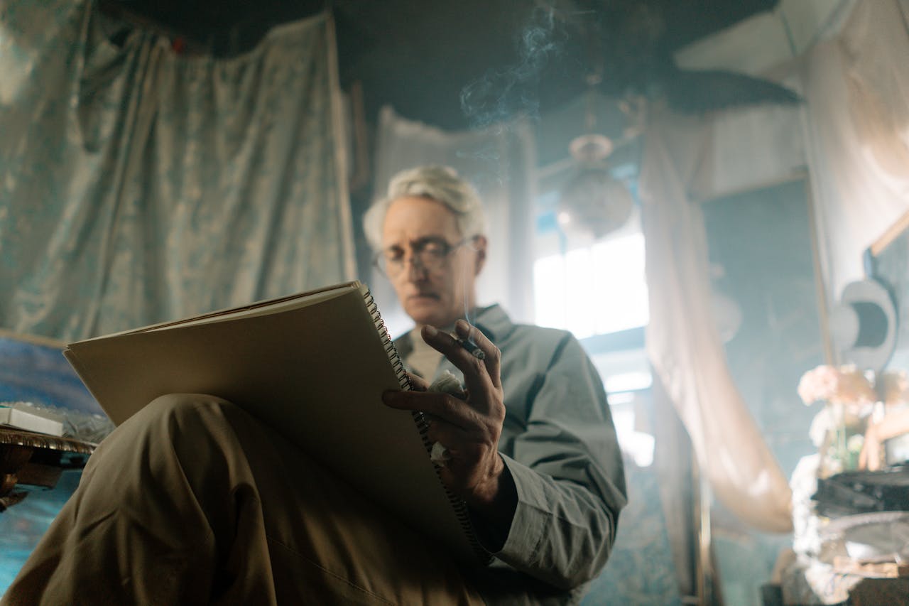 Senior man artist smoking and sketching in a creatively lit studio setting.