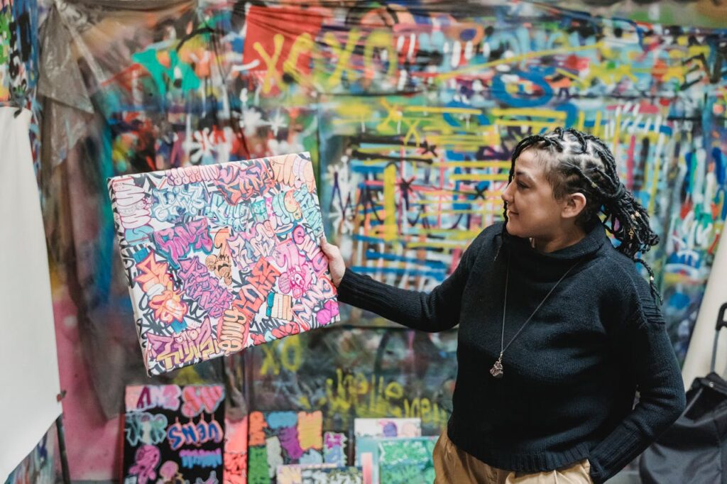 Female artist in studio with bright graffiti art piece, showcasing creativity and urban style.